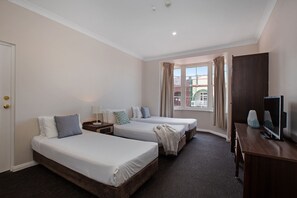 Ein Hotelzimmer mit zwei Betten, einem Schreibtisch, einem Fernseher und einem fensterbepflanzten Fenster.