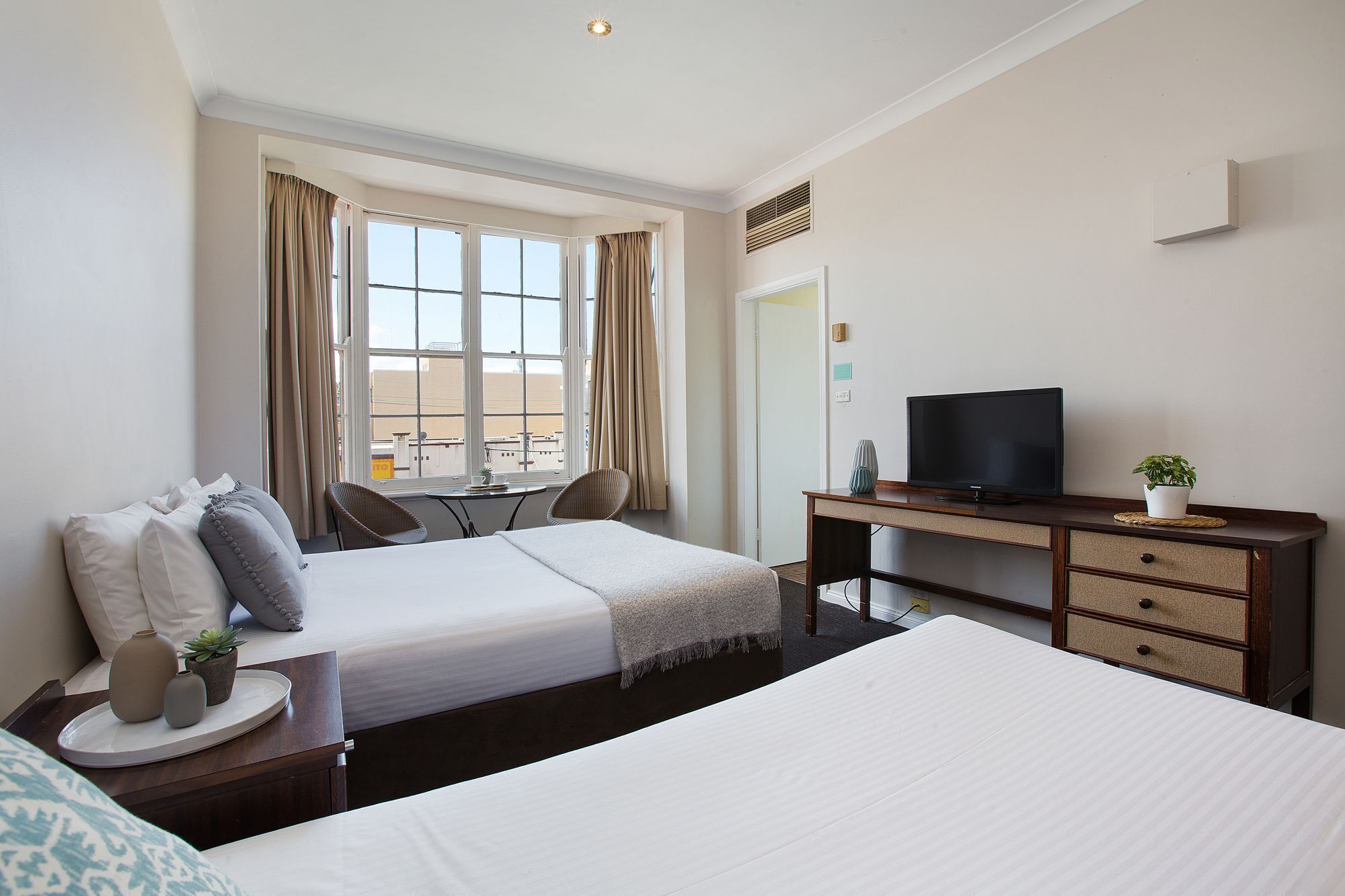 A hotel room with two beds, a desk with a TV, and a window with curtains.