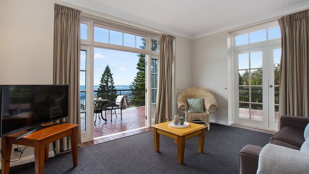 A hotel room with a large window, a television, a wicker chair, and a sofa. - Coogee Bay Hotel Pub Style (Sydney)