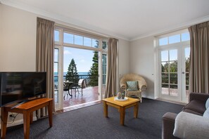 Ein Hotelzimmer mit großem Fenster, Fernseher, Korbsessel und Sofa.