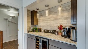 A modern kitchen with a built-in wine cooler, a coffee maker, and a 'CHEERS' sign on the countertop. - Oceans 20 | 480 ft. to the beach | Private Pool, Hot Tub (Virginia Beach)