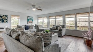 A spacious living room with a ceiling fan, large windows, and a view of neighboring houses. - Oceans 20 | 480 ft. to the beach | Private Pool, Hot Tub (Virginia Beach)