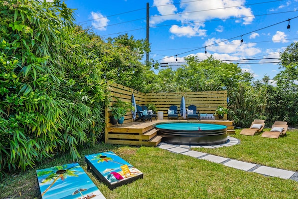 A backyard with a hot tub, lounge chairs, and a wooden deck.