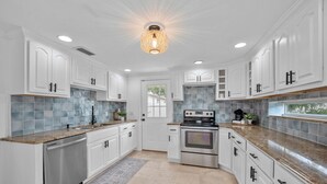 A modern kitchen with white cabinetry, a stainless steel dishwasher, a built-in oven, and a granite countertop.