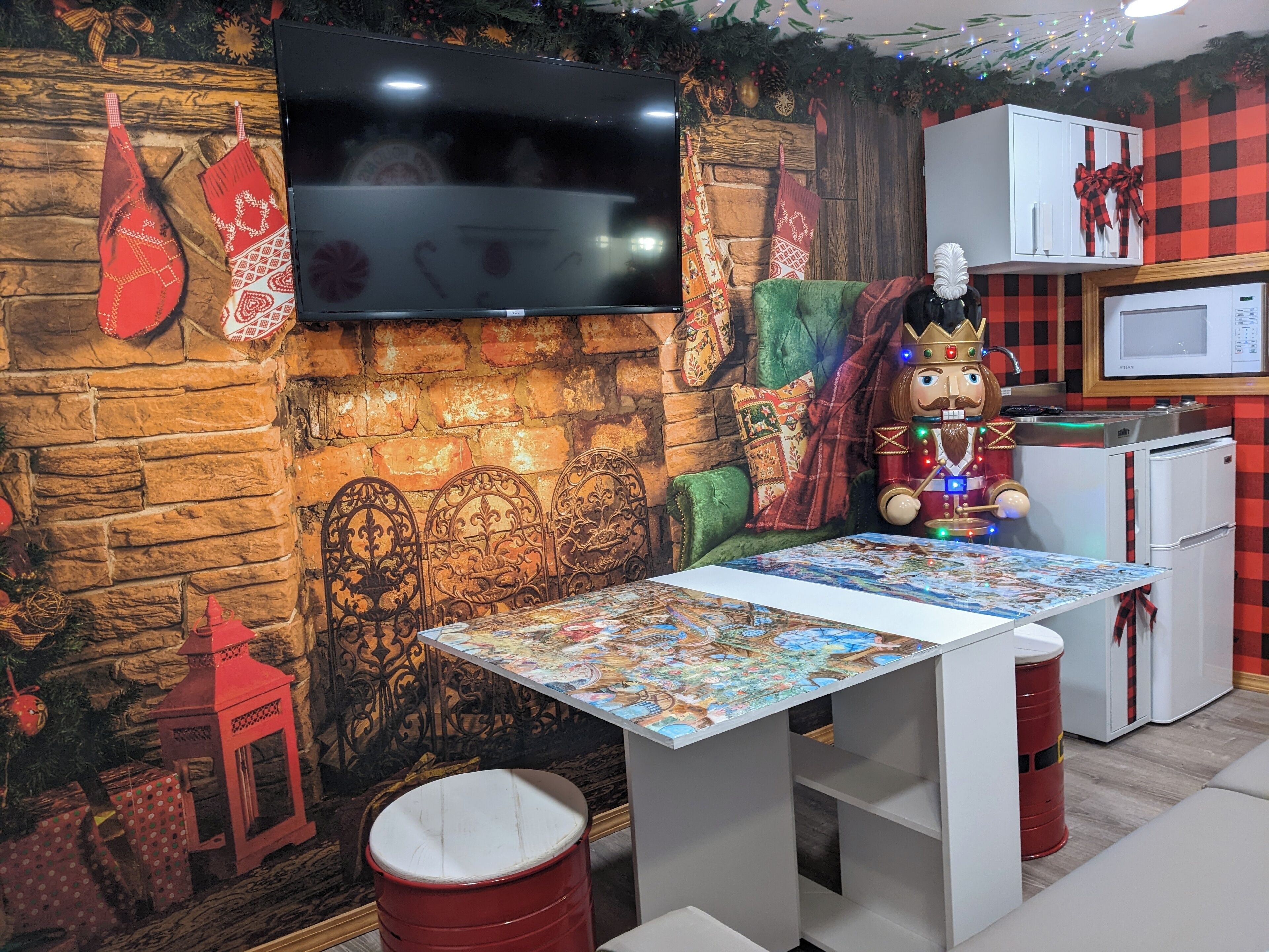 A cozy room with a stone wall, a flat-screen TV, a table with a puzzle, a plush green chair, a red barrel, and a decorative figure.
