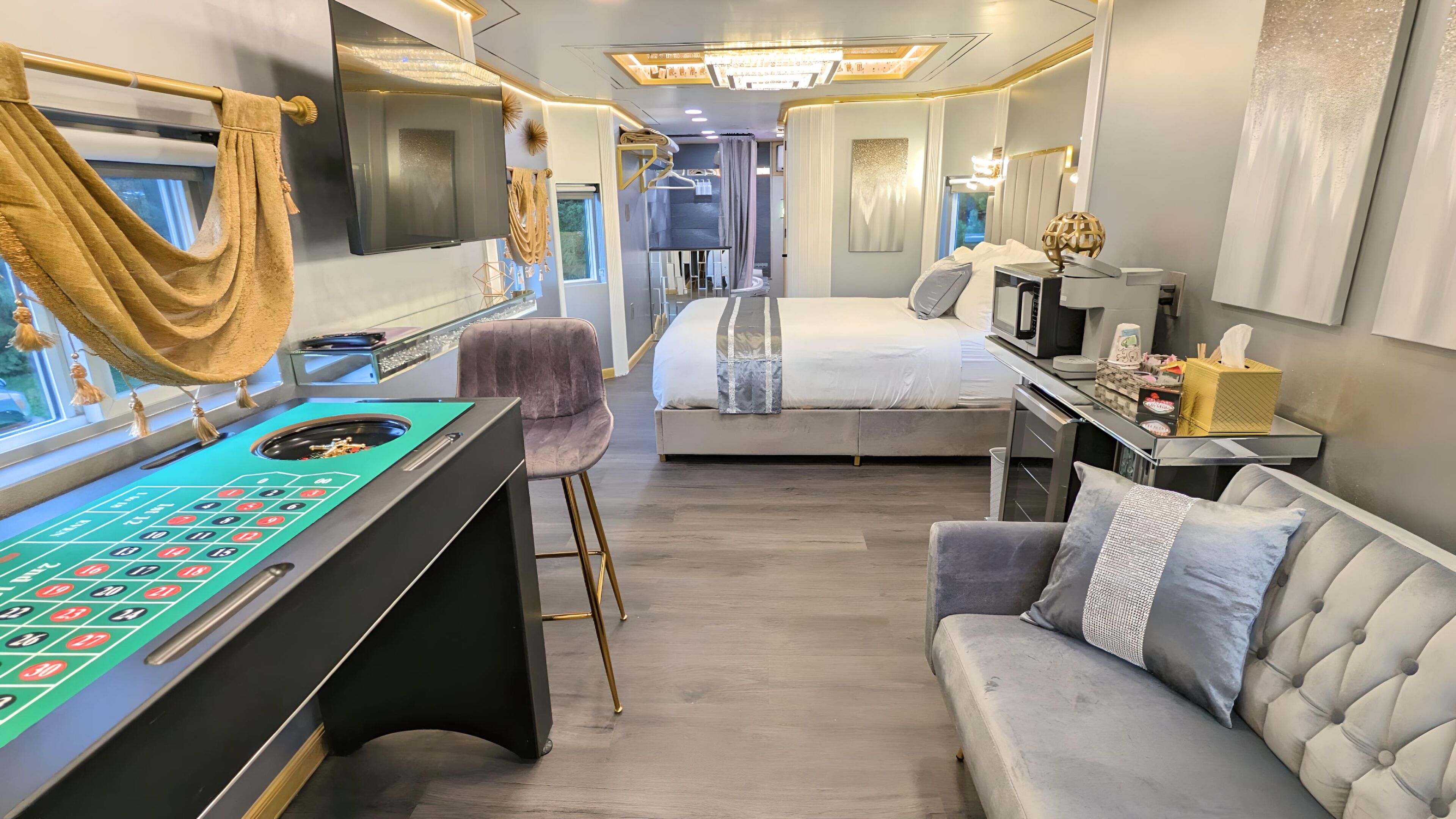 A modern interior with a roulette table, a bed, a sofa, and a desk with a lamp.