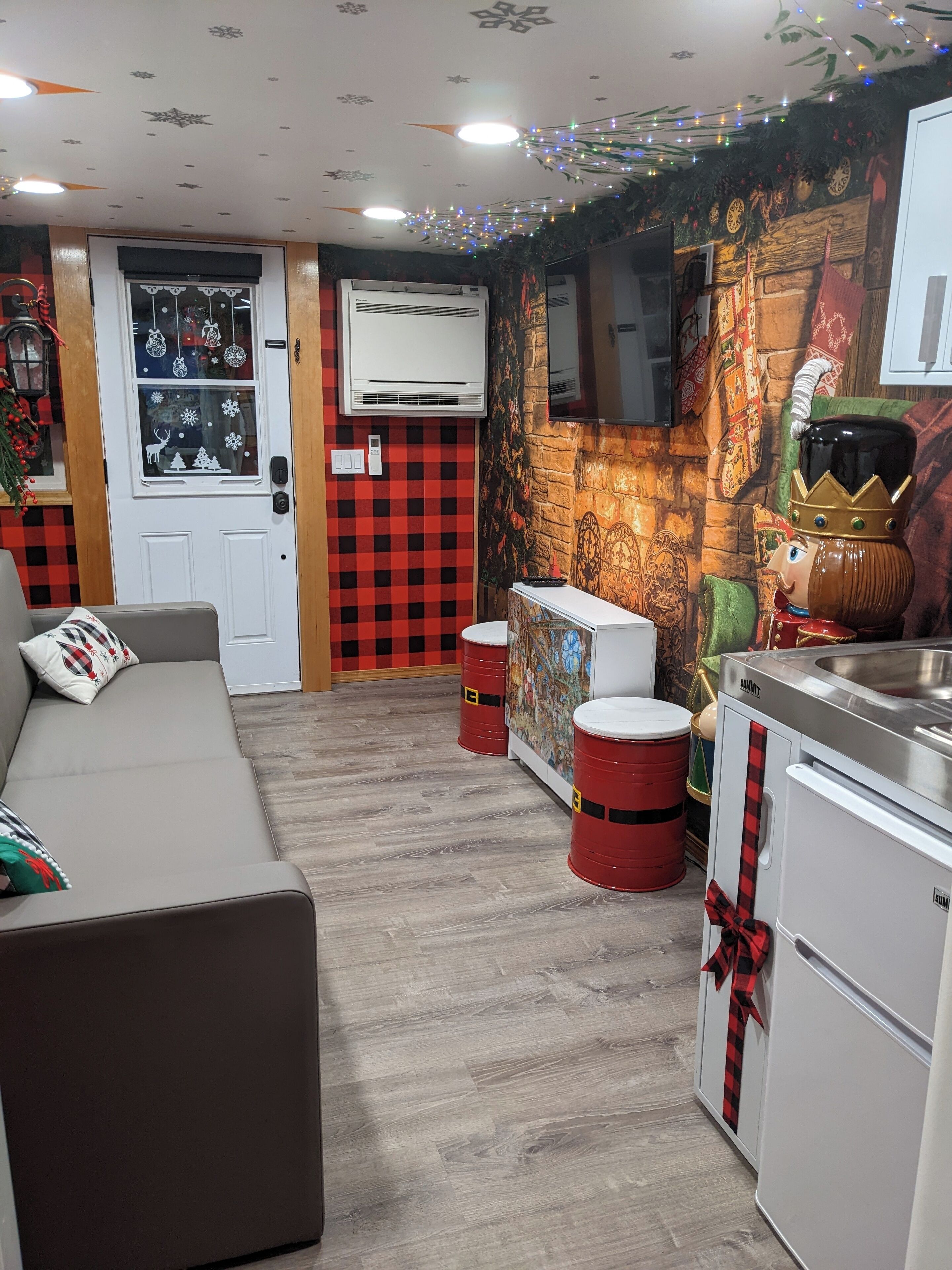 A cozy living room with a sofa, a small kitchen area with a fridge and a stove, and a decorative wall with a mural.