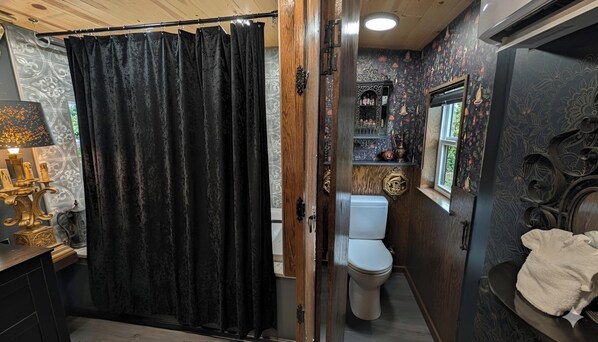 A bathroom with a toilet, a shower curtain, and a vanity with a mirror. - Olympic Railway Inn (Sequim)