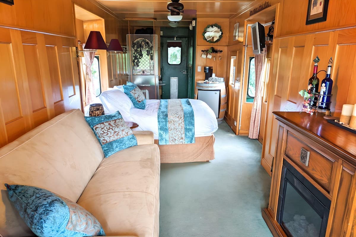 A cozy interior with a sofa, a bed, a small refrigerator, and a wooden cabinet with bottles.