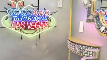 Et badeværelse på et hotel med et neonskilt, der siger "Welcome to Fabulous Las Vegas", et stort spejl med lys og en rund vask med dekorativ fod.