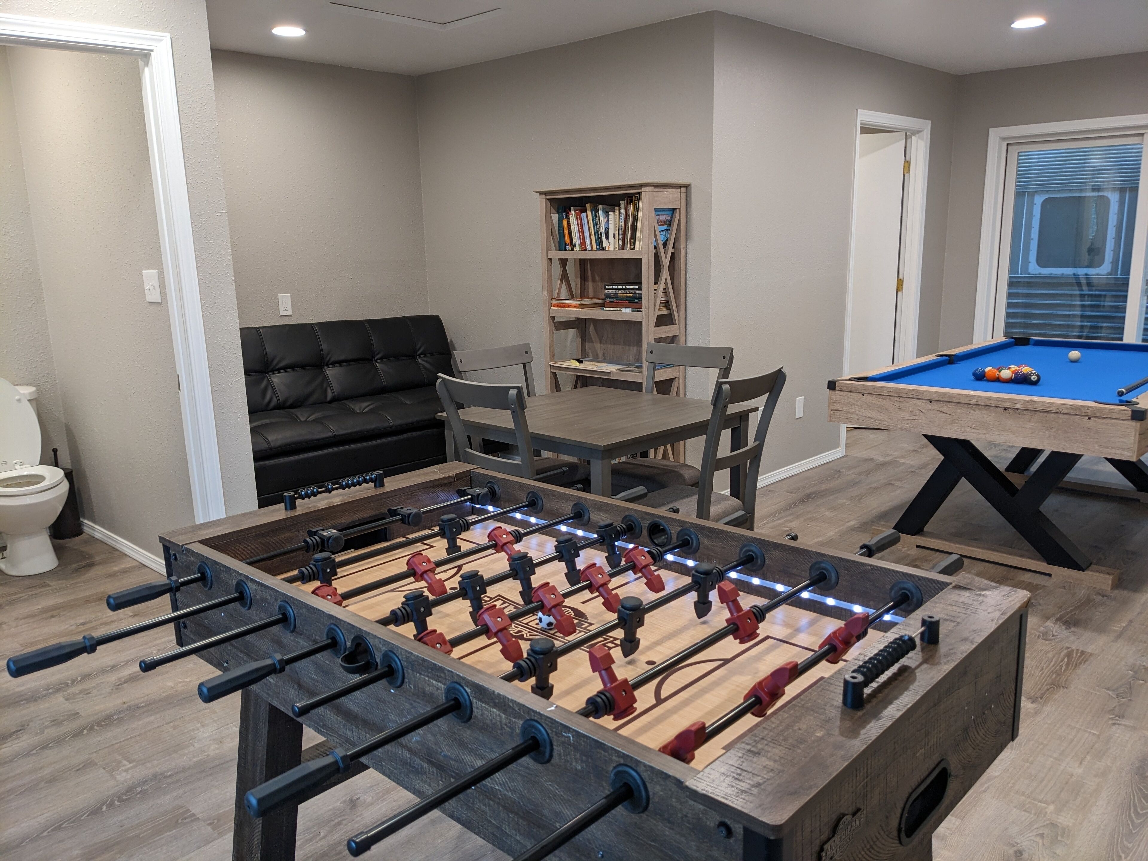 Una habitación con mesa de futbolín, mesa de billar, sofá y estantería.