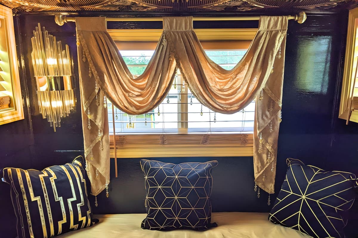 A room with a bed, a window with curtains, and a wall-mounted light fixture.