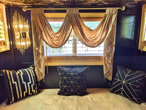 A room with a bed, a window with curtains, and a wall-mounted light fixture.