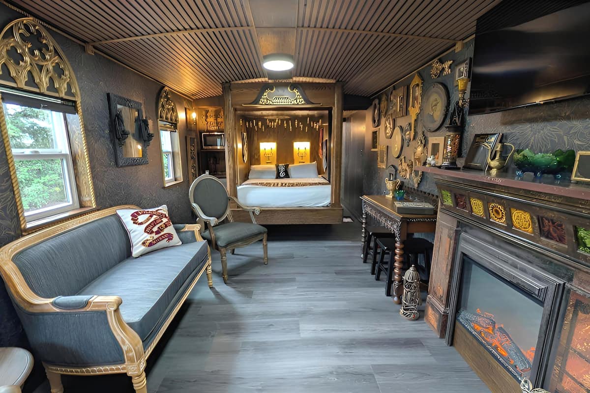 A narrow, elegantly decorated room with a bed, a sofa, a fireplace, and a dining area.