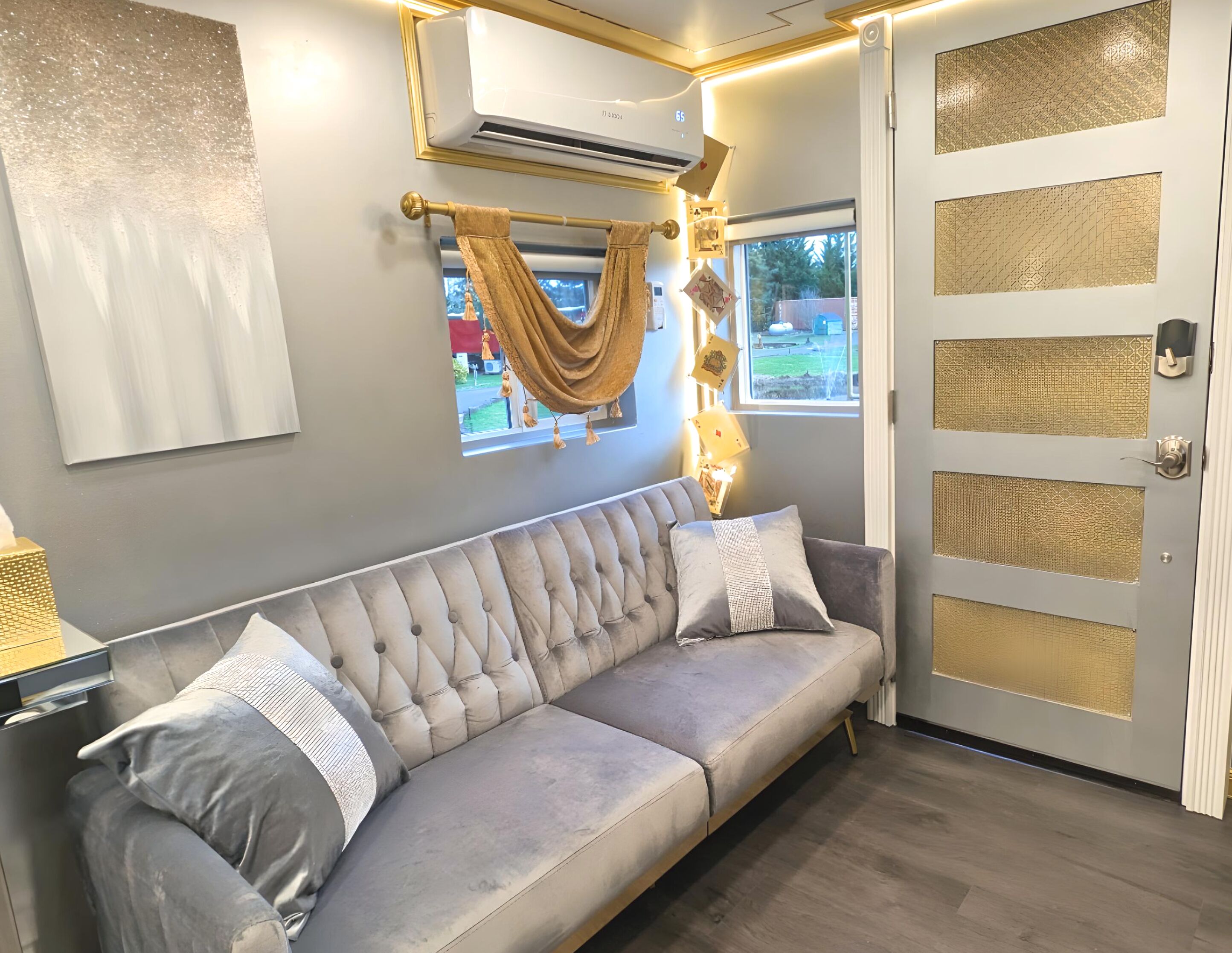 A modern room with a grey sofa, a large window, and a decorative door with patterned panels.