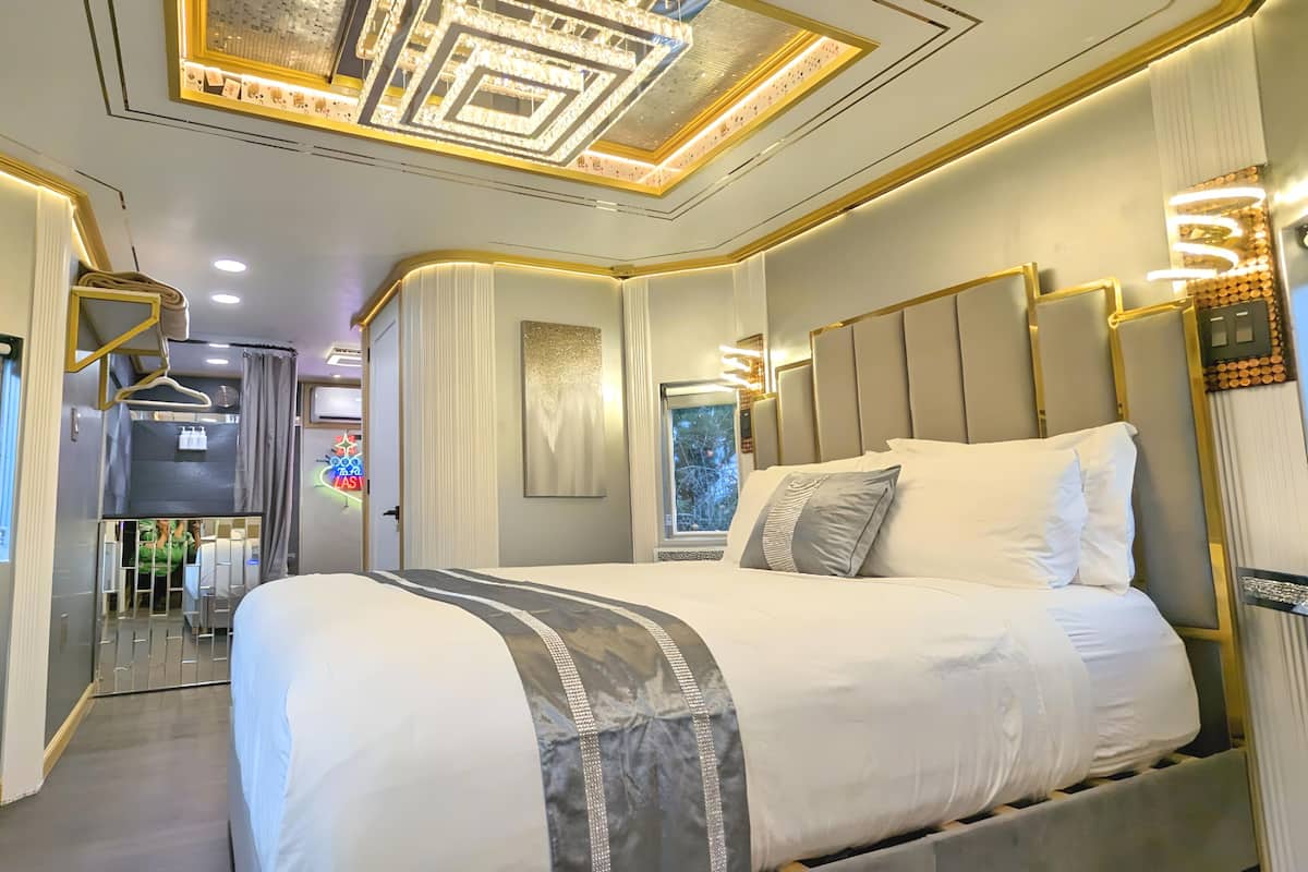 A modern hotel room with a large bed, a vanity with a mirror, and a ceiling with geometric light fixtures.