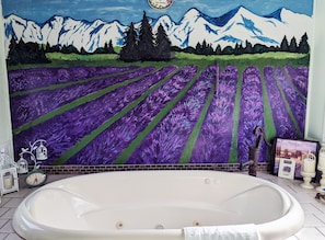 A bathroom with a large bathtub, a mountain landscape mural, and a clock.