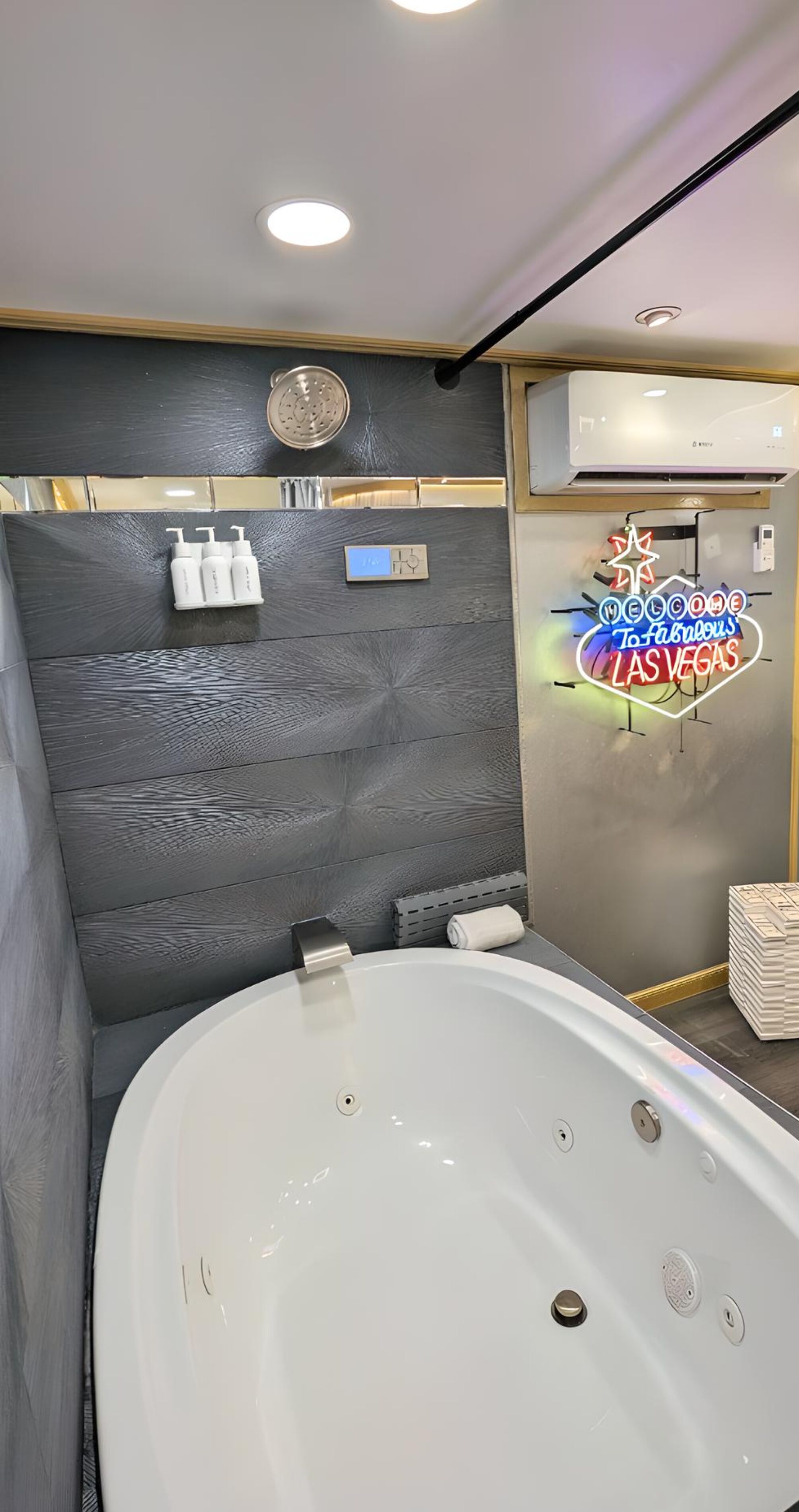 A modern bathroom with a large bathtub, a showerhead, and a neon sign welcoming to Las Vegas.