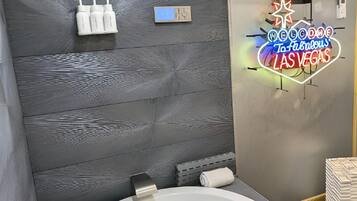 A modern bathroom with a large bathtub, a showerhead, and a neon sign welcoming to Las Vegas.
