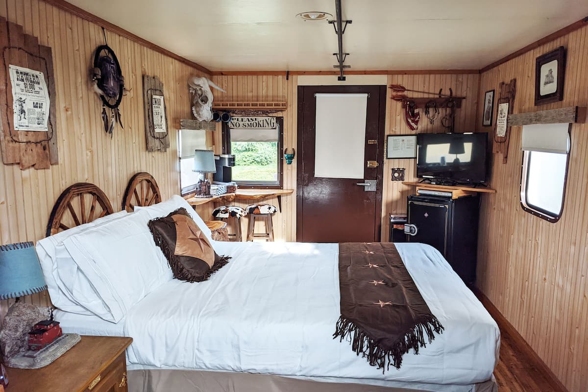 A cozy room with a bed, a desk, a TV, and a window.