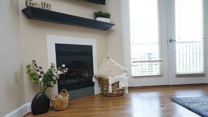 A room with a fireplace, a basket with a house-shaped cover, and a vase with plants.