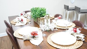A dining table set with white plates, woven placemats, and red and white decorations.