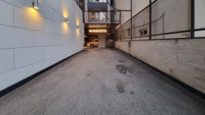 A narrow, concrete-floored corridor with a hound hotel sign, white tiled walls, and a metal fence on one side. - Hound Hotel Seomyeon-bumcheon (Busan)