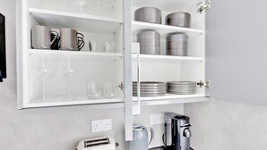 Una cocina con un armario empotrado que contiene copas de vino, platos y utensilios de cocina.