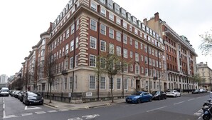 Un edificio de varios pisos con entrada en esquina, un letrero que dice 'Goodwood Court' y autos estacionados a lo largo de la calle.