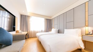 Quarto de hotel com duas camas, uma escrivaninha, uma cadeira e uma janela grande com cortinas.