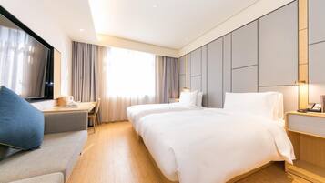 Quarto de hotel com duas camas, uma escrivaninha, uma cadeira e uma janela grande com cortinas.