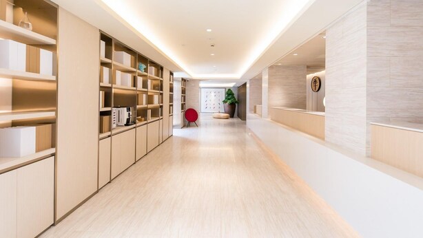 A modern hotel corridor with built-in shelving, a reception desk, and a seating area with a red chair. - Ji Hotel Shanghai Stadium (Shanghai)