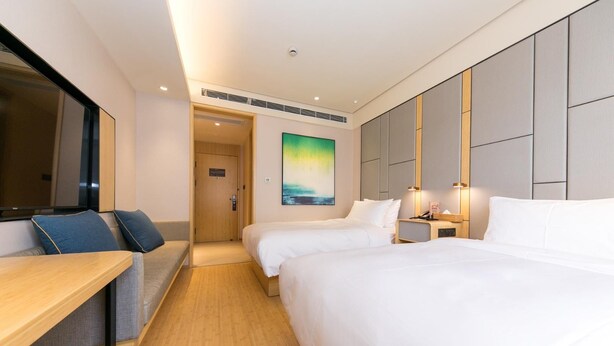 Quarto de hotel com duas camas, uma mesa, um sofá e um quadro na parede.