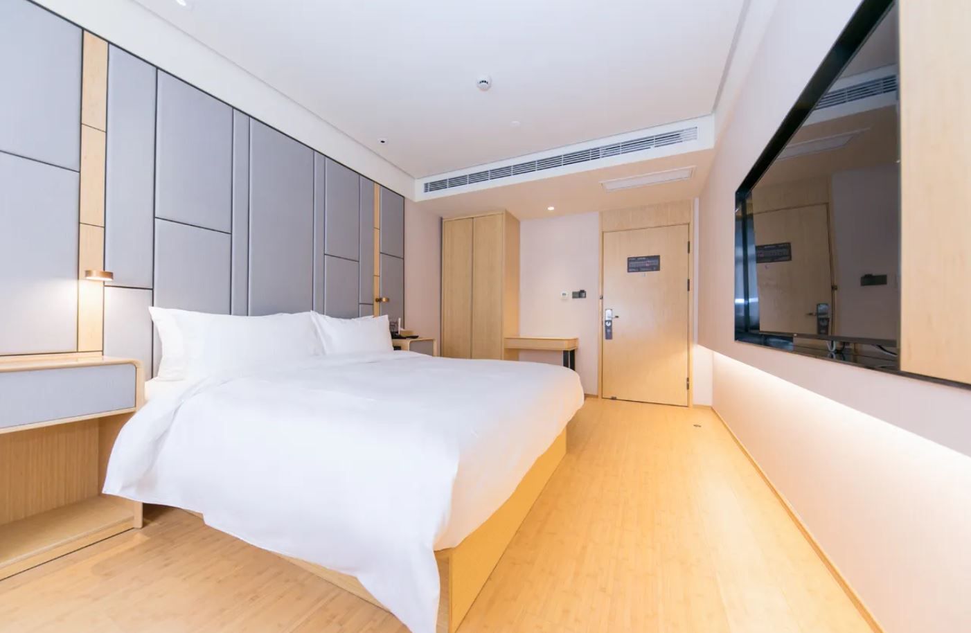 Una habitación de hotel moderna con una cama grande, armario empotrado y un espejo amplio.