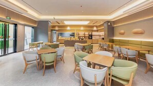 Um restaurante moderno com decoração contemporânea, área de bar central, diversos arranjos de assentos e cozinha visível ao fundo.
