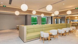 Um hall moderno com um sofá verde, mesas redondas e iluminação pendente.