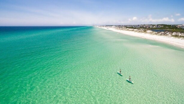 Vue aérienne d’une plage aux eaux turquoise et limpides et au rivage sablonneux.