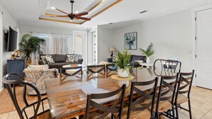 Un vaste salon doté d’une table à manger en bois, de chaises sombres et d’un ventilateur de plafond.