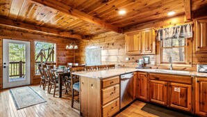 L’intérieur d’un chalet en bois comprend une cuisine, un coin repas et une grande fenêtre donnant sur une forêt.