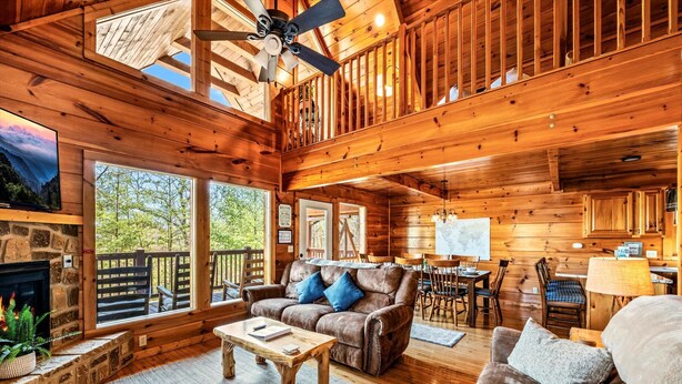Une cabane en bois spacieuse, dotée d’un salon confortable, de grandes fenêtres et d’une cheminée.