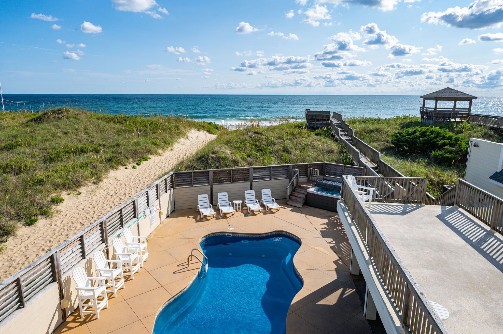 Un espace piscine aménagé au bord de la plage, avec des chaises longues, une petite piscine et un belvédère offrant une vue sur l’océan.