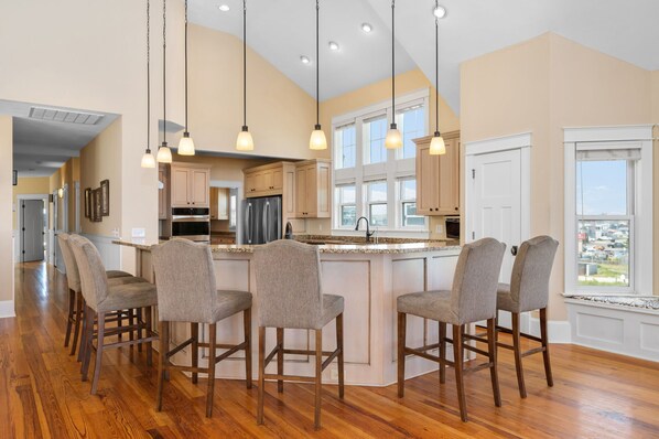 A spacious kitchen with a large island, wooden bar stools, and pendant lighting.
