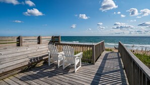 Une terrasse en bois avec des chaises blanches donnant sur une plage.