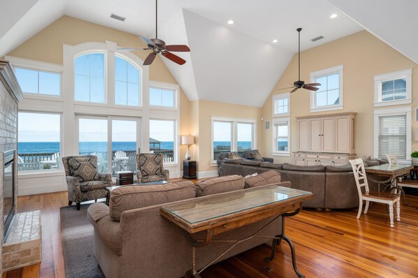 A spacious living room with a large glass table, multiple seating options, and a view of the ocean.