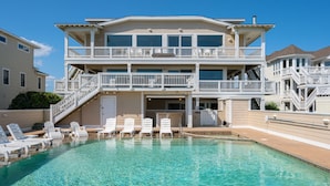 A two-story building with a pool, multiple balconies, and outdoor seating. - Take It to the Limit: 16 Bedrooms, oceanfront, pool, elevator, hot tubs, rec room, theater room! (Nags Head)