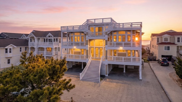 A multi-story residential building with a central entrance, balconies, and a driveway. - Take It to the Limit: 16 Bedrooms, oceanfront, pool, elevator, hot tubs, rec room, theater room! (Nags Head)