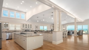 A spacious kitchen with a large island, white cabinetry, and a view of the ocean. - Take It to the Limit: 16 Bedrooms, oceanfront, pool, elevator, hot tubs, rec room, theater room! (Nags Head)