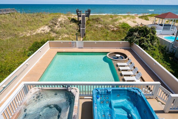 Una piscina en la azotea con hidromasaje, sillas de descanso y vista a la playa y al océano.