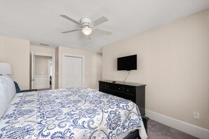 Quarto com cama, ventilador de teto, televisão e porta.