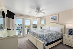Un dormitorio con cama, ventilador de techo, mesita de noche, escritorio y vistas al exterior.